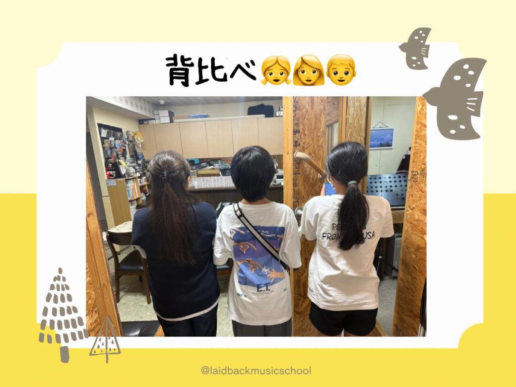 小6の生徒ちゃんと先生が並んで背比べをしている後ろ姿。教室での成長を感じる一コマ。